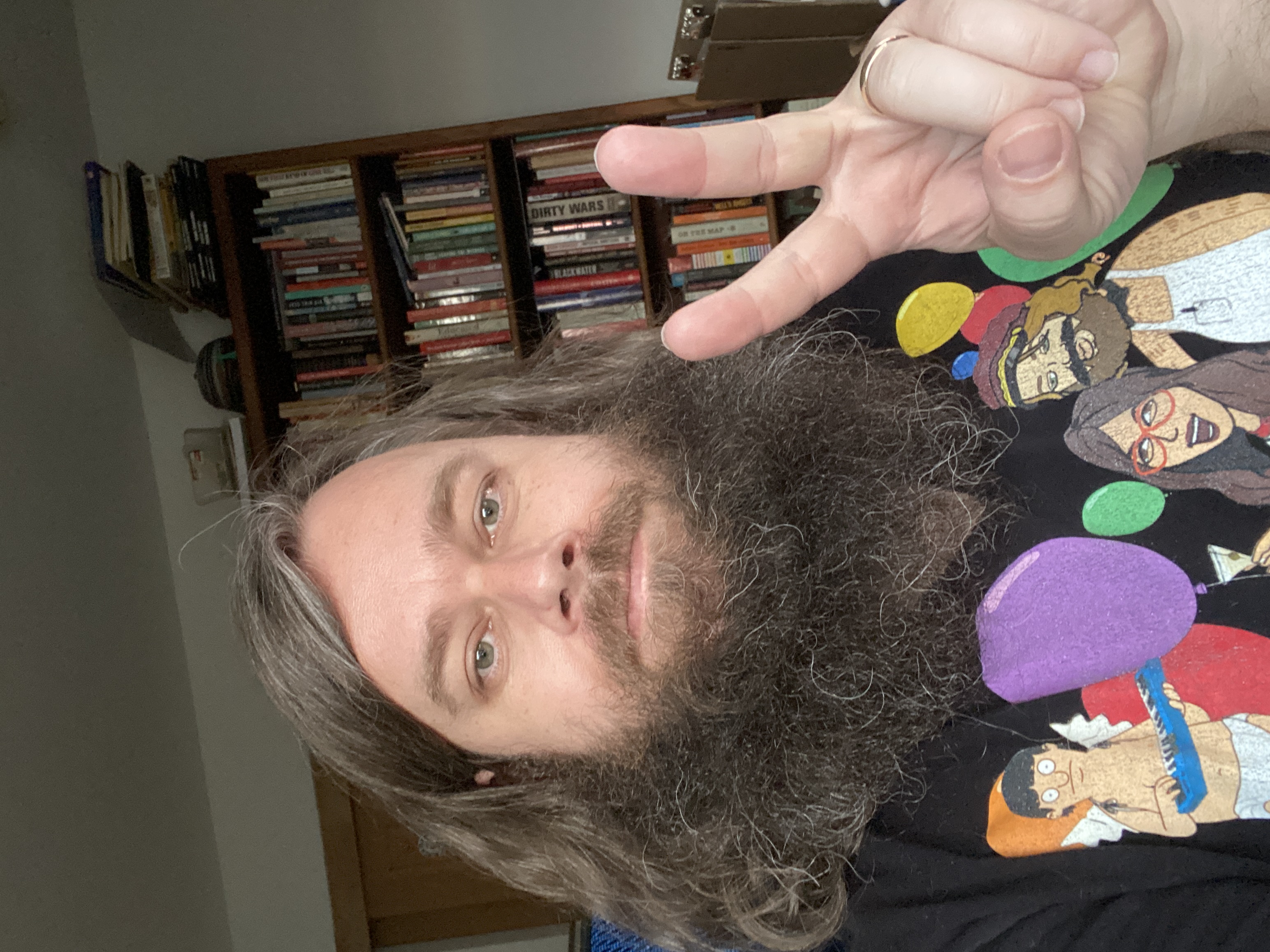 picture of me in a bobs burgers shirt giving a peace sign. I have a beard and long hair and am smiling!