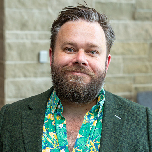 picture of a handsome man with a nice smile wearing a green suit jacket and a green button up shirt with small yellow flowers on it.